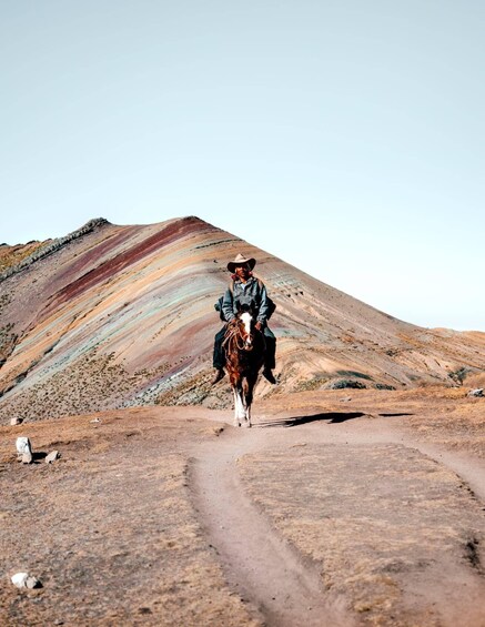 A person riding a horse on a dirt path with a colorful mountain in the background. 5