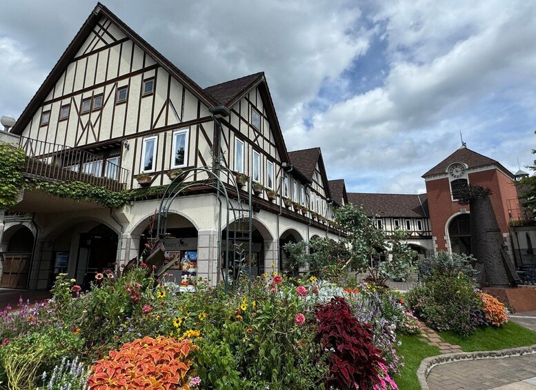 A traditional half-timbered building with a clock tower, surrounded by a well-maintained garden with various colorful flowers. 1