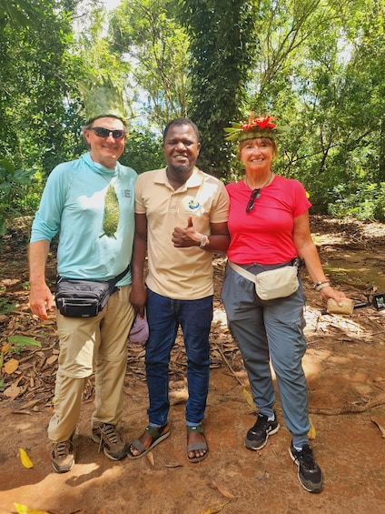 Three people standing outdoors in a forested area with trees and a dirt ground. 3