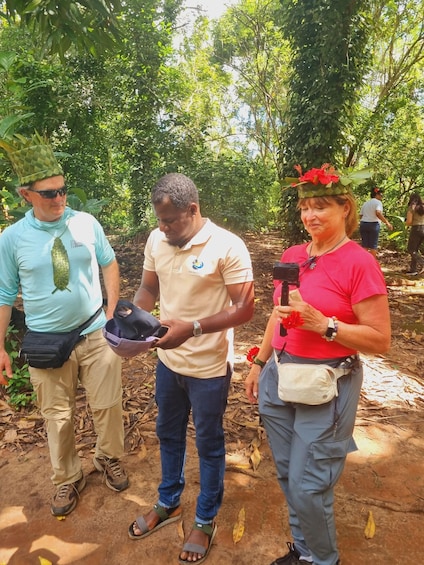 Three people in a forested area, one holding a hat and another holding a camera. 2