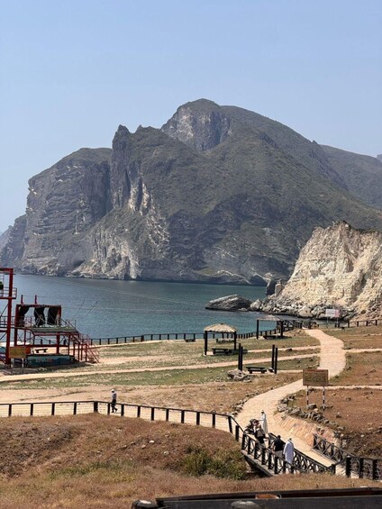 A coastal landscape with a prominent cliff, a lifeguard tower, and a walking path. 4