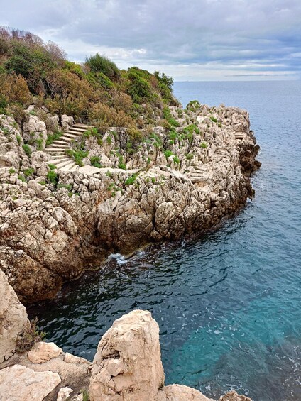 A rocky coastline with a staircase leading down to the water, surrounded by vegetation and a clear sky. 2