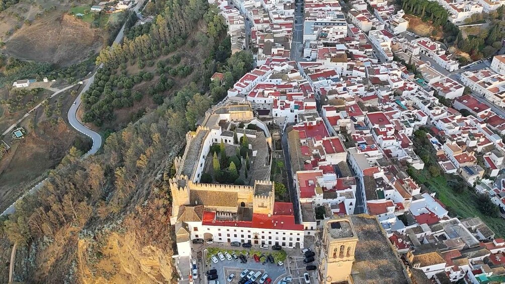 An aerial view of a town with a prominent castle-like structure surrounded by red-roofed buildings, a winding road, and a river. 5