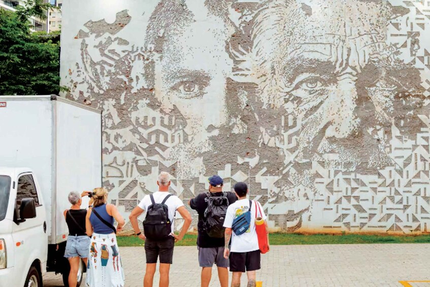A group of people standing in front of a large mural with geometric patterns. 2