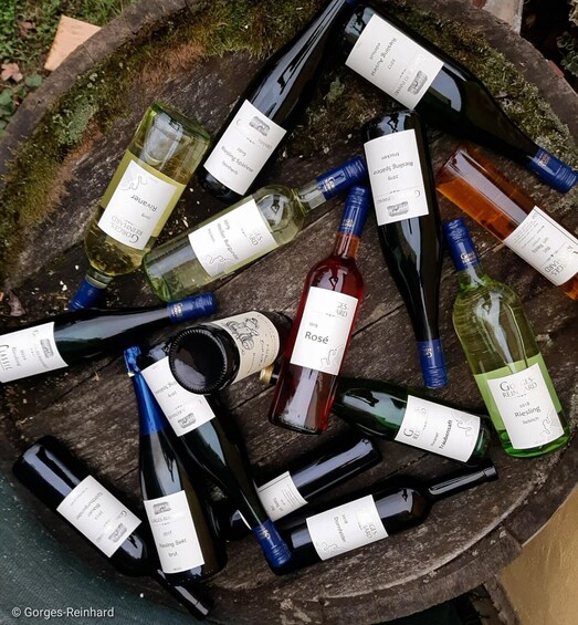 A collection of wine bottles with labels, some in a wooden barrel. 1