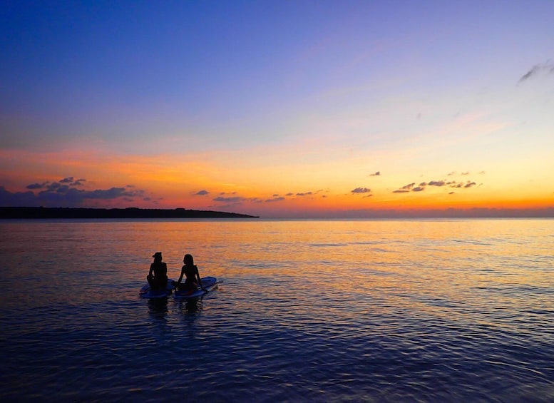 A sunset over a calm sea with two people on paddleboards. 1
