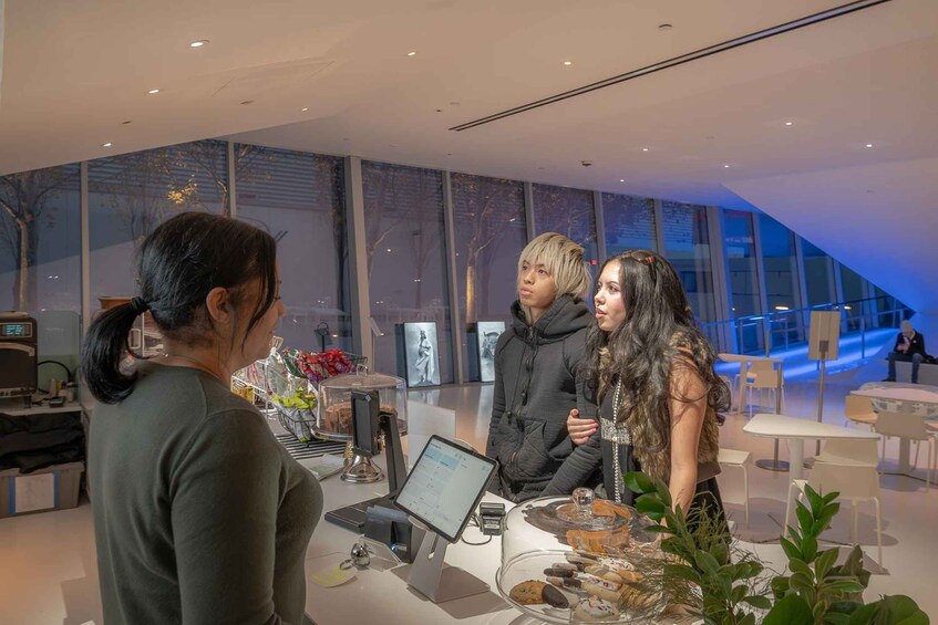 A modern interior with a glass display case containing pastries, a digital kiosk, and a seating area with tables and chairs. 5