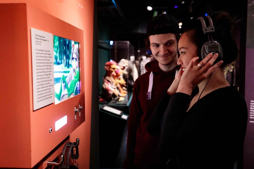 A person using a smartphone with headphones, standing in front of an informational display with text and images. 1