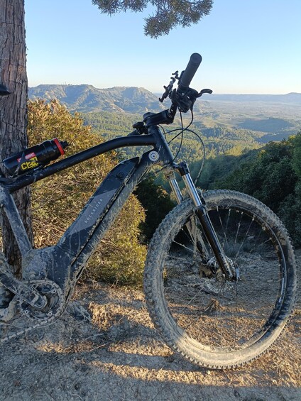 A mountain bike parked on a dirt path with a scenic view of a forested valley and distant hills. 3