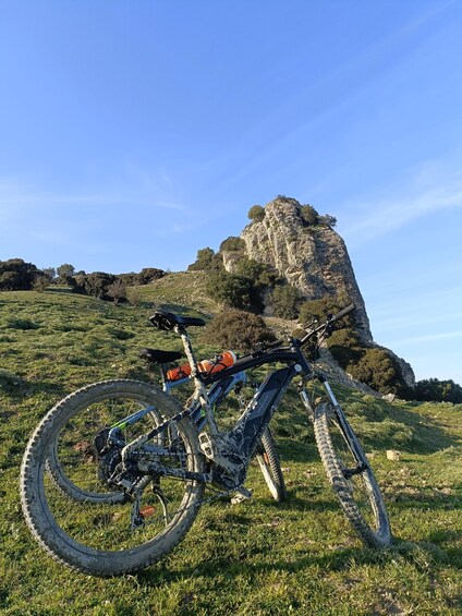 A mountain bike parked on grass with a rocky hill in the background. 1
