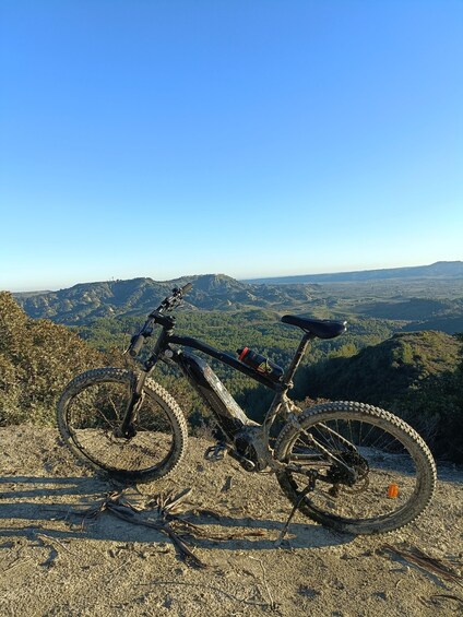 A mountain bike parked on a rocky terrain with a scenic view of a valley and distant hills. 2