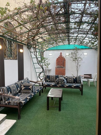 An outdoor seating area with patterned sofas and a small table, surrounded by greenery and a decorative wall. 1