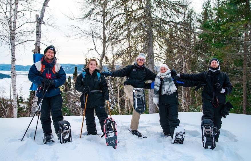 A group of people standing on a snowy slope with ski equipment, surrounded by trees and a distant view of mountains. 2