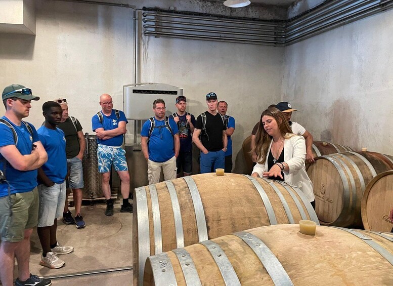 A group of people in a wine cellar with wooden barrels and a large industrial cooler. 5