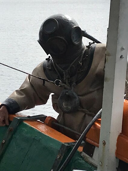 A person in a diving suit and helmet, seated in a boat. 2