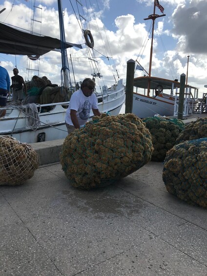 A man handling large nets on a dock with boats in the background. 5
