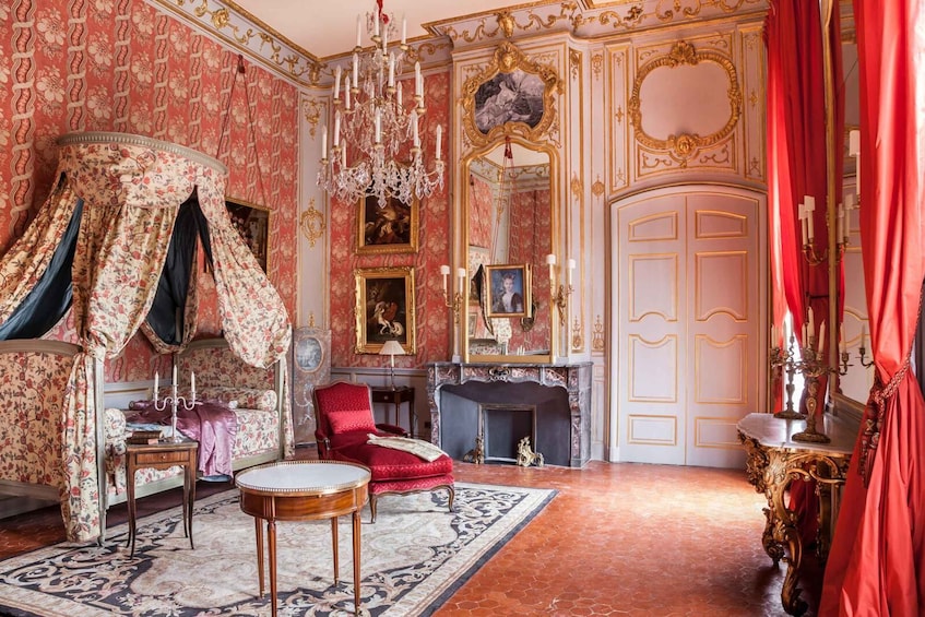 An opulent room with ornate wallpaper, a red armchair, a chandelier, and a fireplace. 5