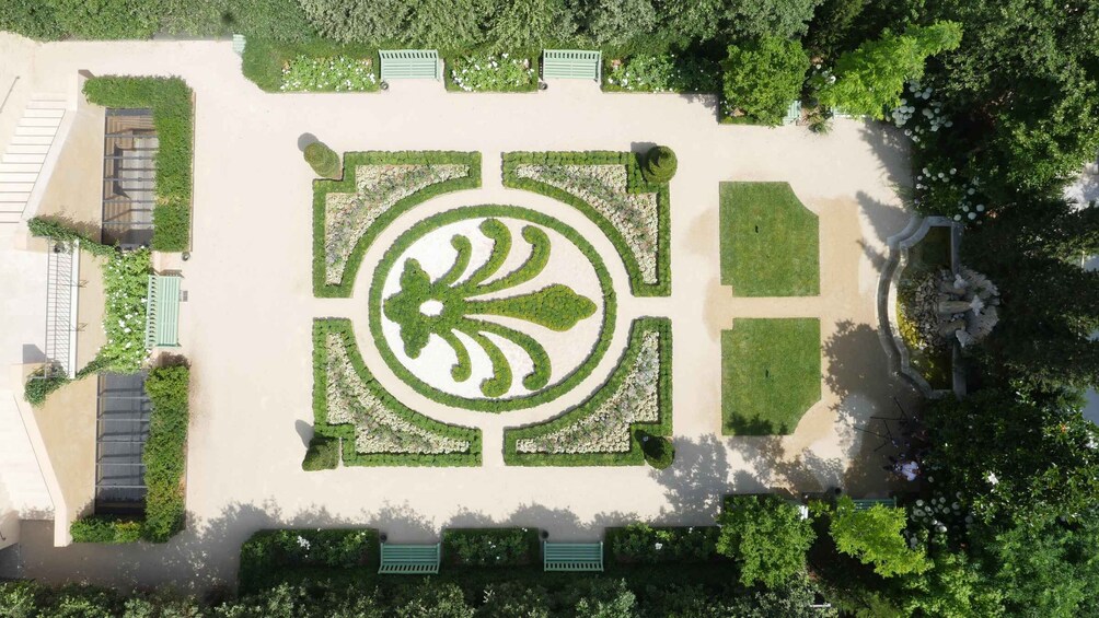 An aerial view of a landscaped garden with a central circular design, bordered by green hedges and a paved walkway. 5