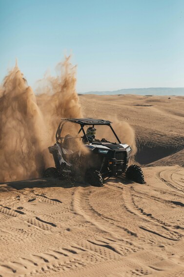 A Polaris ATV driving through a desert with sand being kicked up by its tires. 4