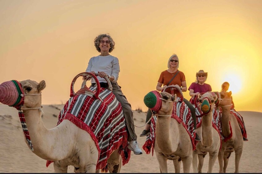 Four people riding camels in a desert at sunset. 5