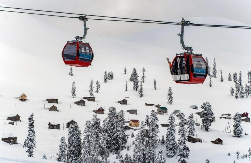 Two red ski lifts with cabins, a snowy mountain landscape, and small wooden cabins scattered across the slope. 1
