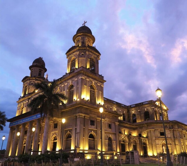 A historic building with two domes and a large central tower, illuminated at dusk. 3