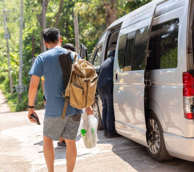 A person walking away from a silver van, carrying a backpack and a plastic bag. 4