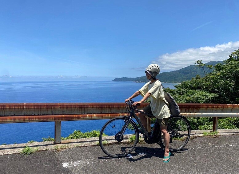 A person riding a bicycle on a road with a view of the ocean and mountains. 5