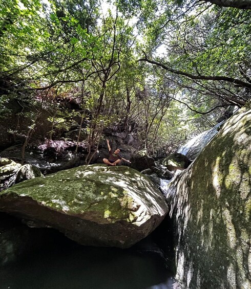 A person meditating on a rock in a forested area with a waterfall in the background. 2