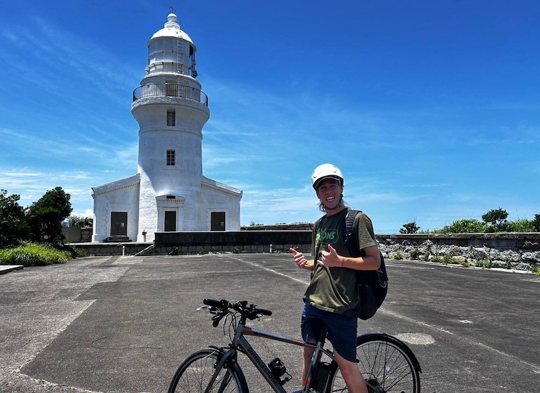 A person standing next to a bicycle with a white lighthouse in the background. 4