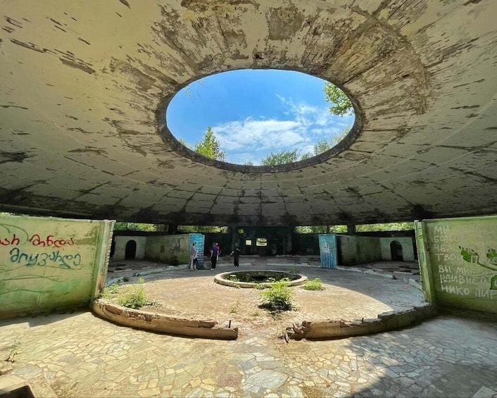 An abandoned building with a circular skylight, graffiti on walls, and a central courtyard with plants. 1