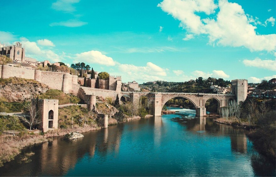 A historic stone bridge over a river, surrounded by ancient walls and a town. 2