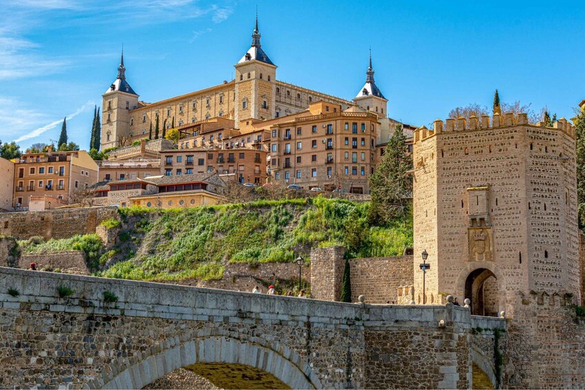 A historic cityscape with a prominent castle, a stone bridge, and a clear blue sky. 1