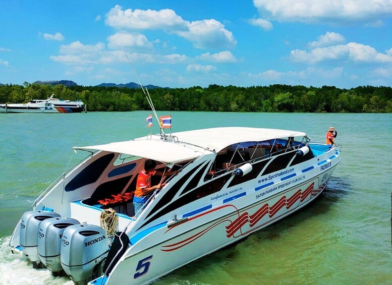 A speedboat with a Thai flag, moving on clear turquoise water with a forested shoreline in the background. 4