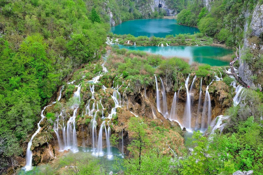 A multi-tiered waterfall cascading into a turquoise lake surrounded by dense green forest. 4