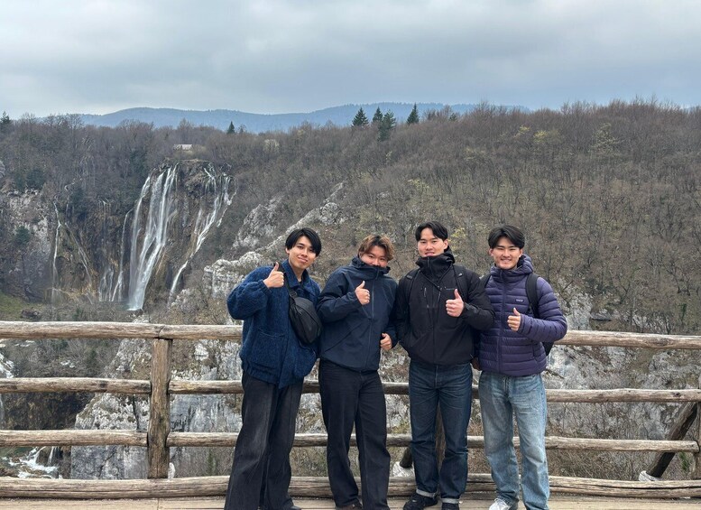 A group of people standing on a wooden bridge with a waterfall in the background. 3