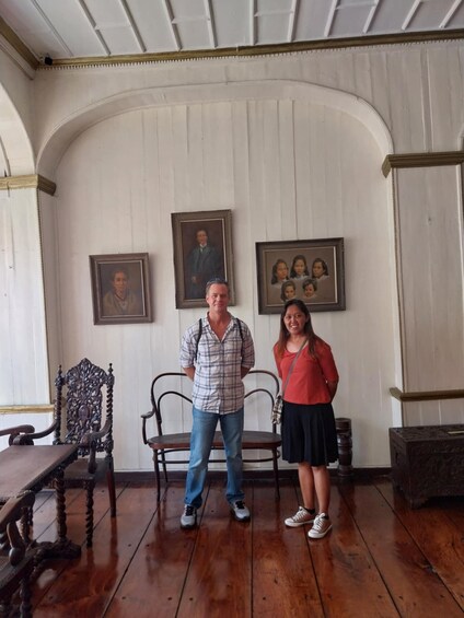 A room with wooden panel walls, a wooden floor, a wooden chair, and a table. There are three framed portraits on the wall. 2