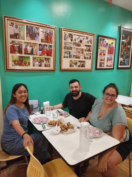 Three people seated at a table with food and drinks, surrounded by framed photographs on the wall. 5