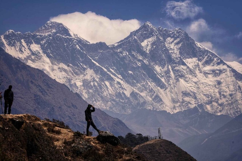 Two people standing on a rocky outcrop with a mountain range in the background. 1