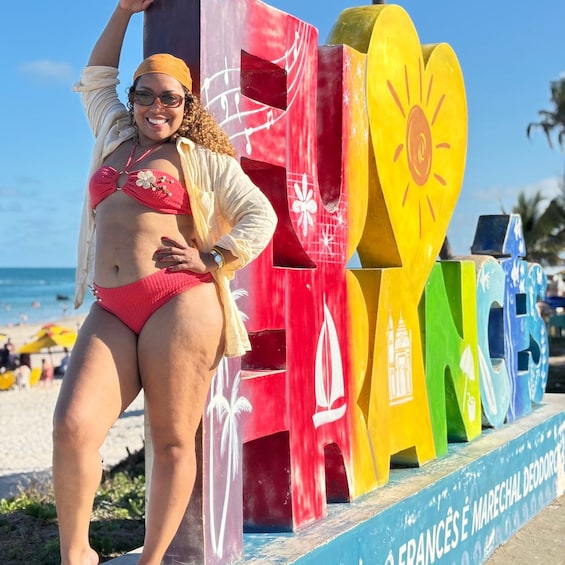A person in a red bikini and yellow headscarf posing in front of colorful letters spelling 'FRANCE' on a beach. 2