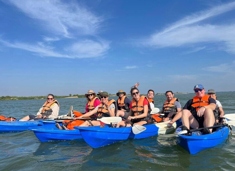 A group of people in blue canoes on a calm body of water, wearing life jackets. 1