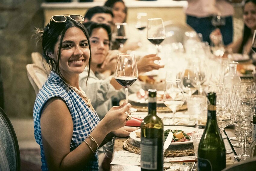A person holding a wine glass at a dining table with multiple wine bottles and glasses. 1