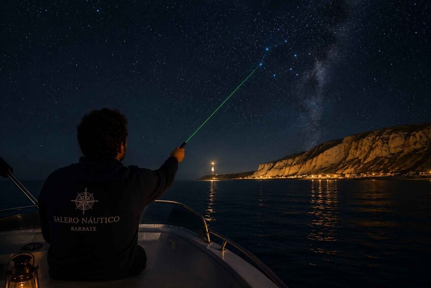 A person on a boat pointing a laser at the stars, with a coastline in the background. 1