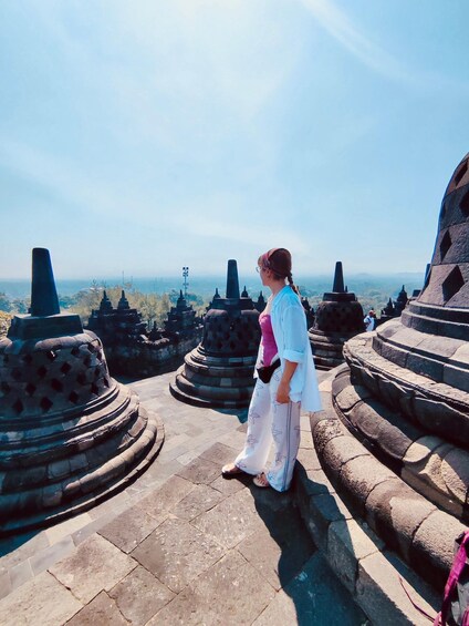 A person standing on a stone pathway with large stone structures in the background. 2