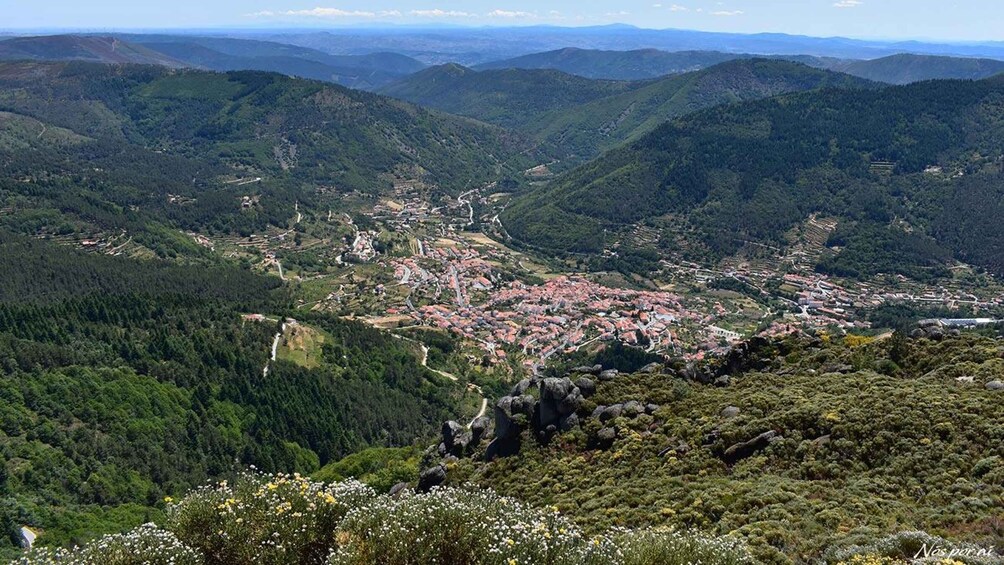 A mountainous landscape with a town nestled in the valley, surrounded by dense forests and rocky outcrops. 3