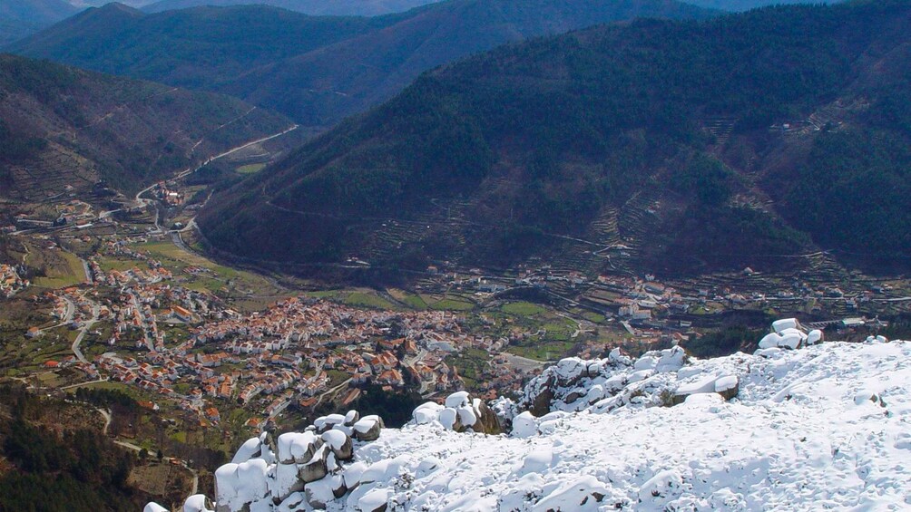 A mountainous landscape with a valley, a town, and snow-covered rocks in the foreground. 2