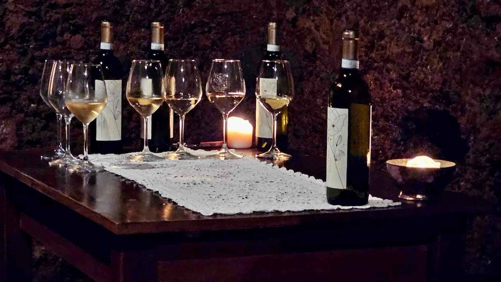 A table with wine bottles and glasses, a lit candle, and a lace doily. 2