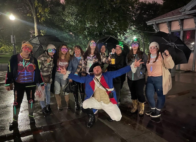 A group of people outdoors at night, some holding umbrellas. 1
