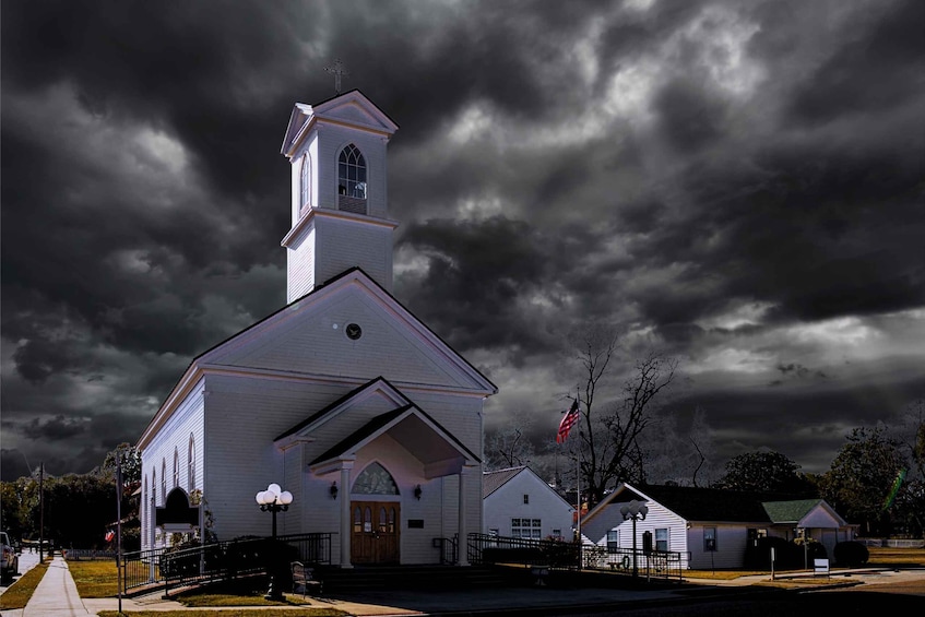 A white church with a steeple and a bell tower, surrounded by a fence and a flag. 1