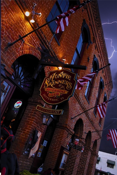 A brick building with a sign for 'Antie Skinners Riverboat Club' and American flags. 2